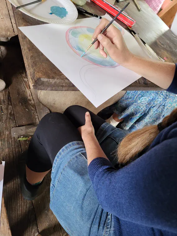 Overhead view of a hand painting pink, teal and yellow rings inside pencil guide circles on paper.