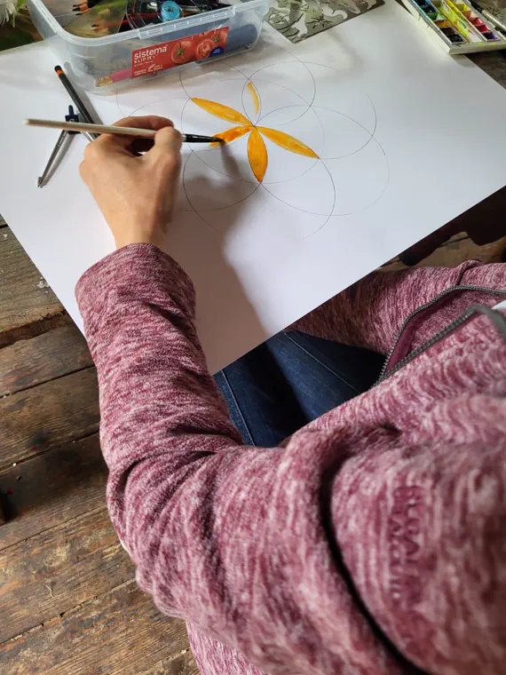 Hand painting orange-gold petals radiating from the centre of a pencil-drawn circle.