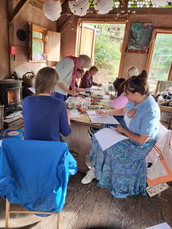 Workshop participants drawing at a long table in a timber barn, with Karen standing at the head of the table.